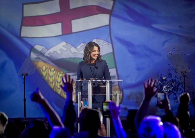 Danielle smiling at her supporters with the Alberta flag in the background